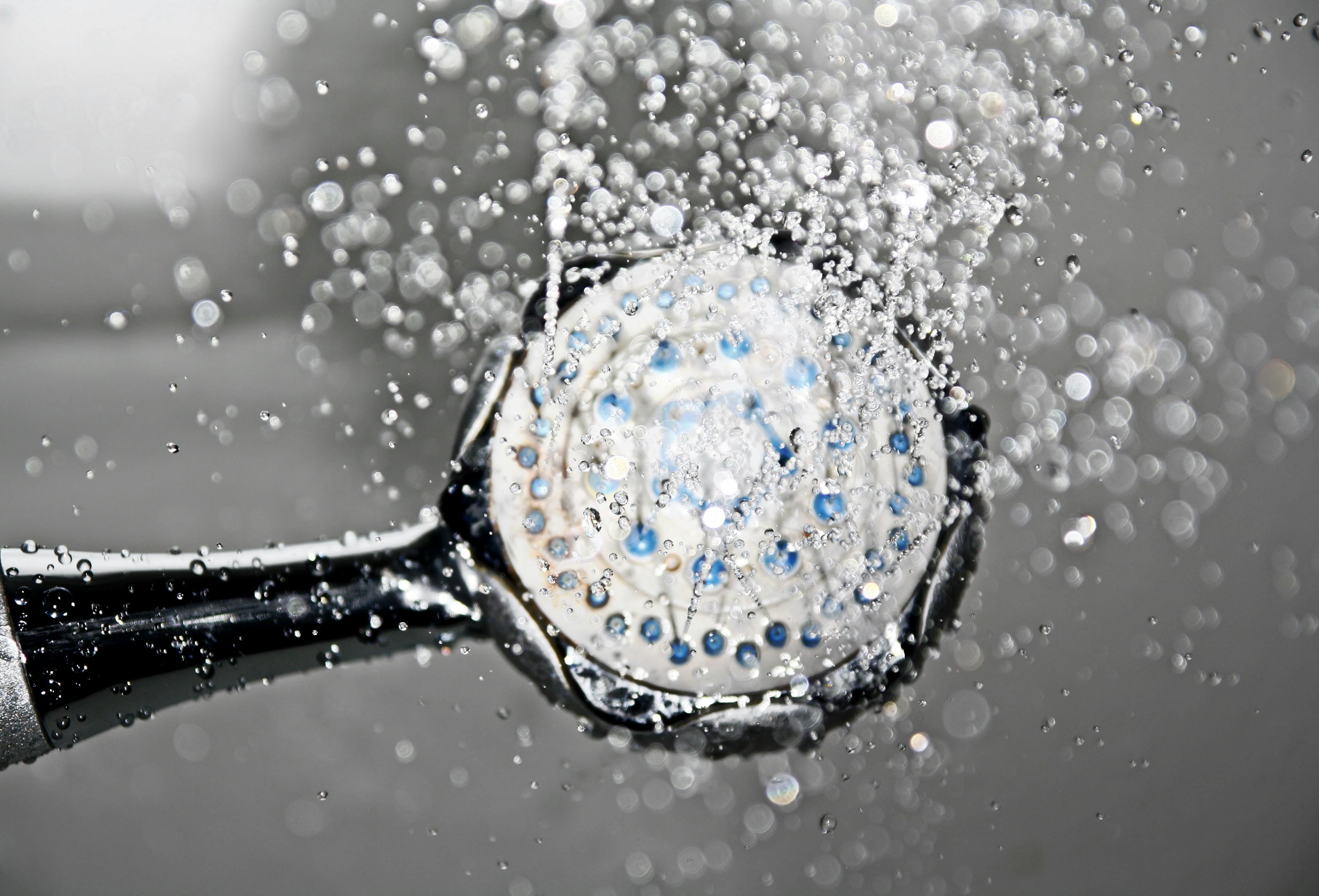 Shower head with running water and fine droplets hanging in the air: the aerosol through which Legionella spreads in showers